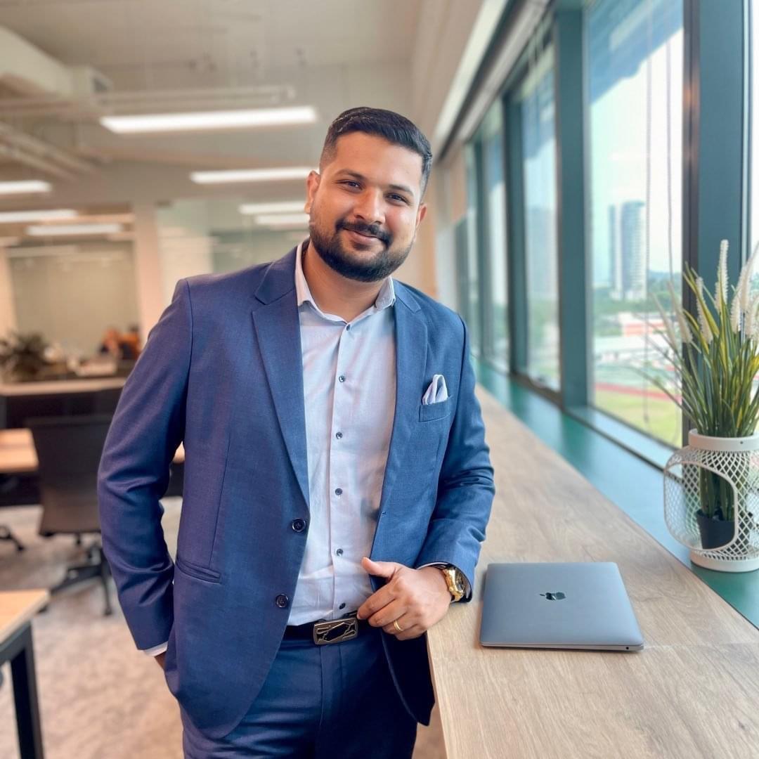 Shyam Prakash in a blue suit standing beside a window